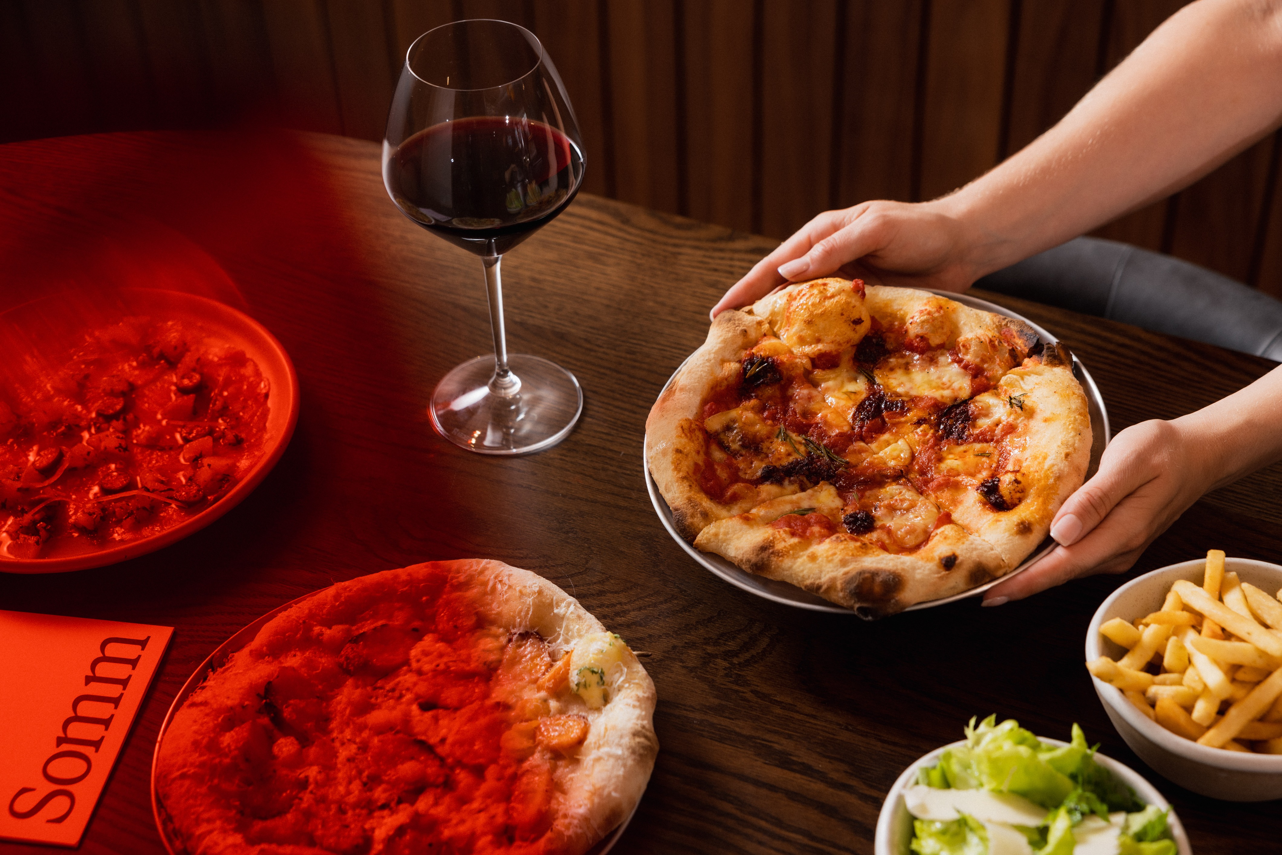 Pizza being placed on a table of food and wine