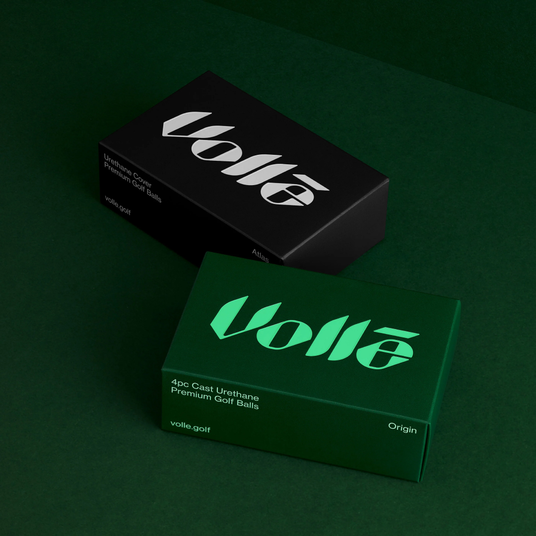 Two volle golf ball boxes, one blakc one green on top of green background