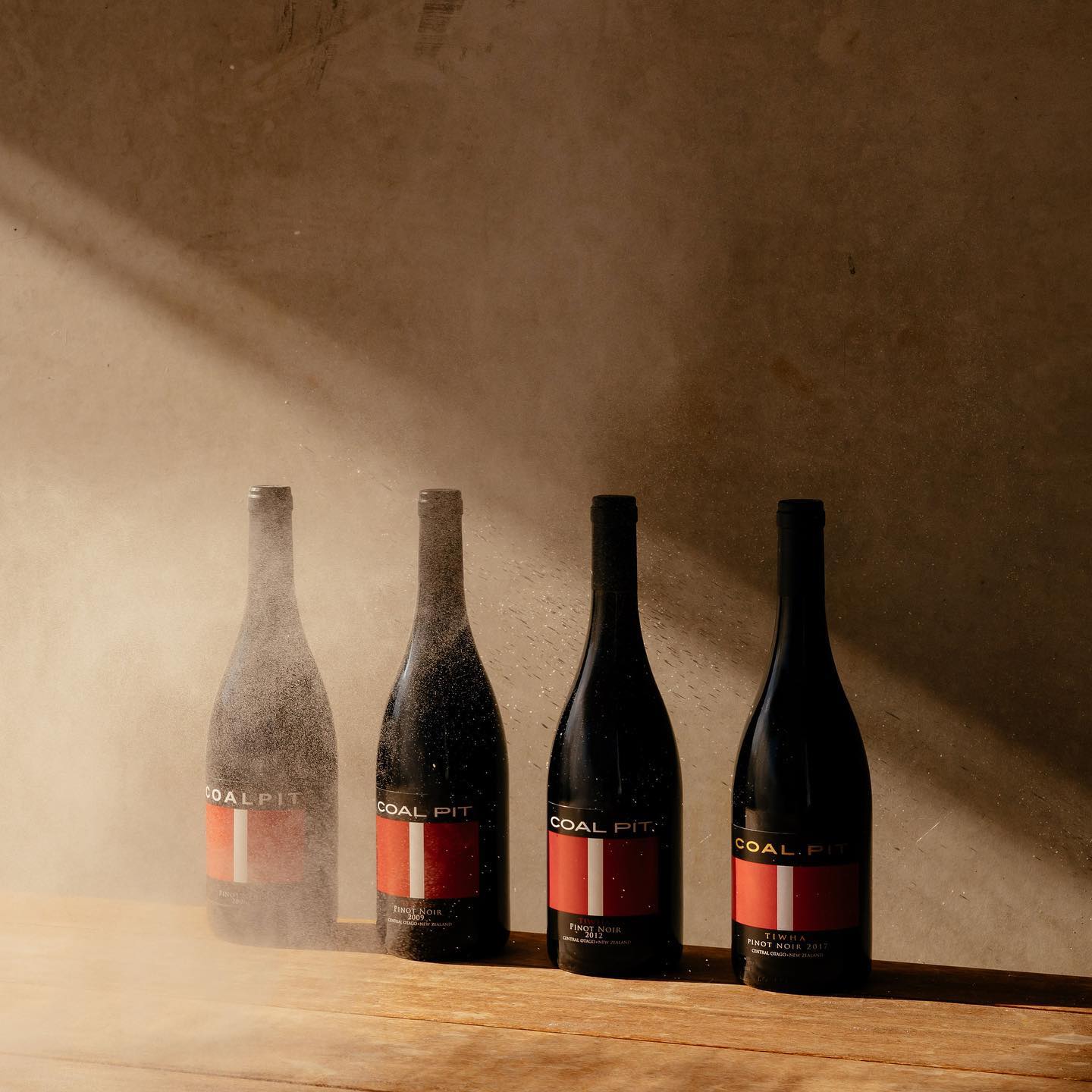 Four Coal Pit wine bottles on wood bench with sunlight shining on them