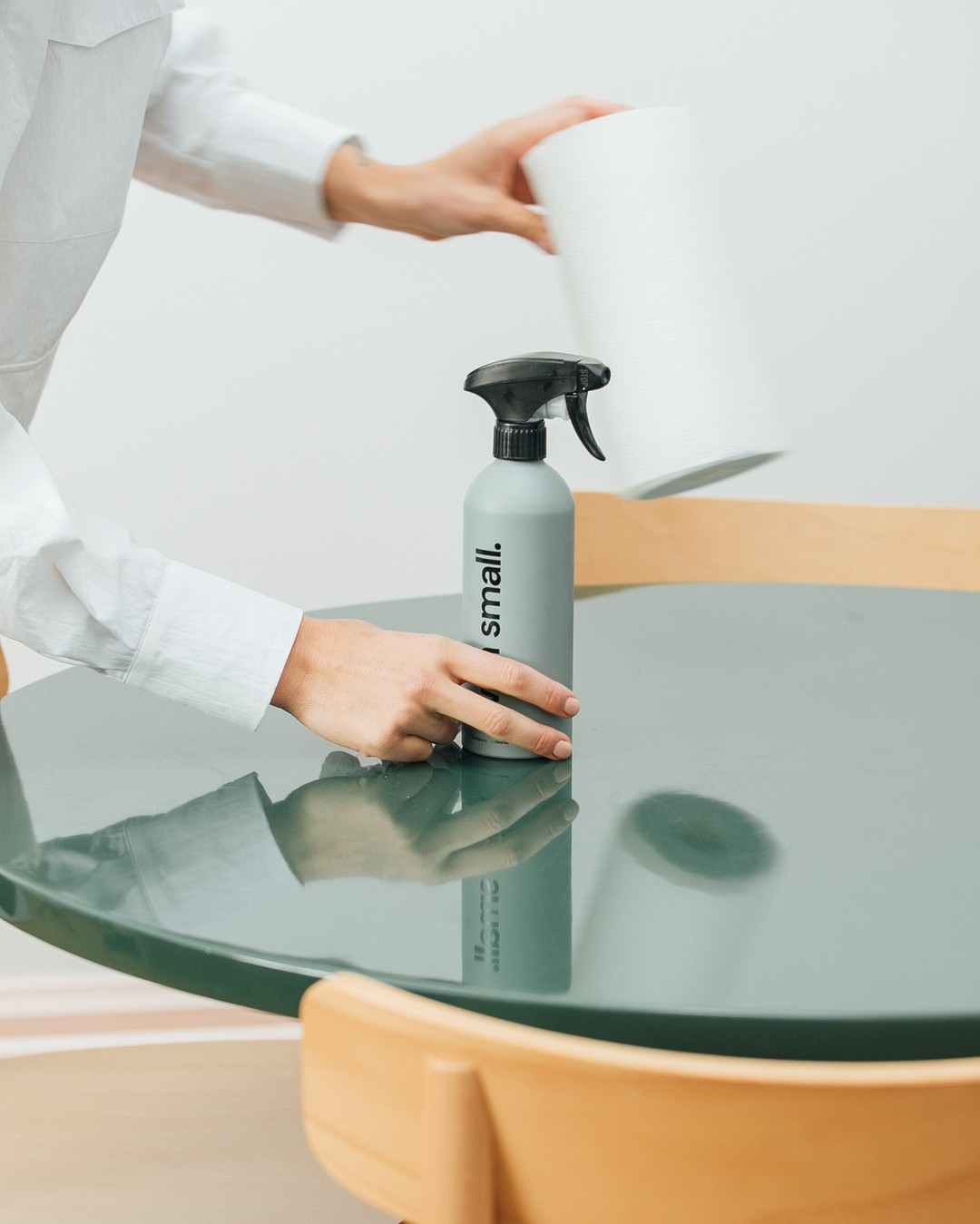 Hands grabbing green With Small spray bottle and paper towels off of a green table